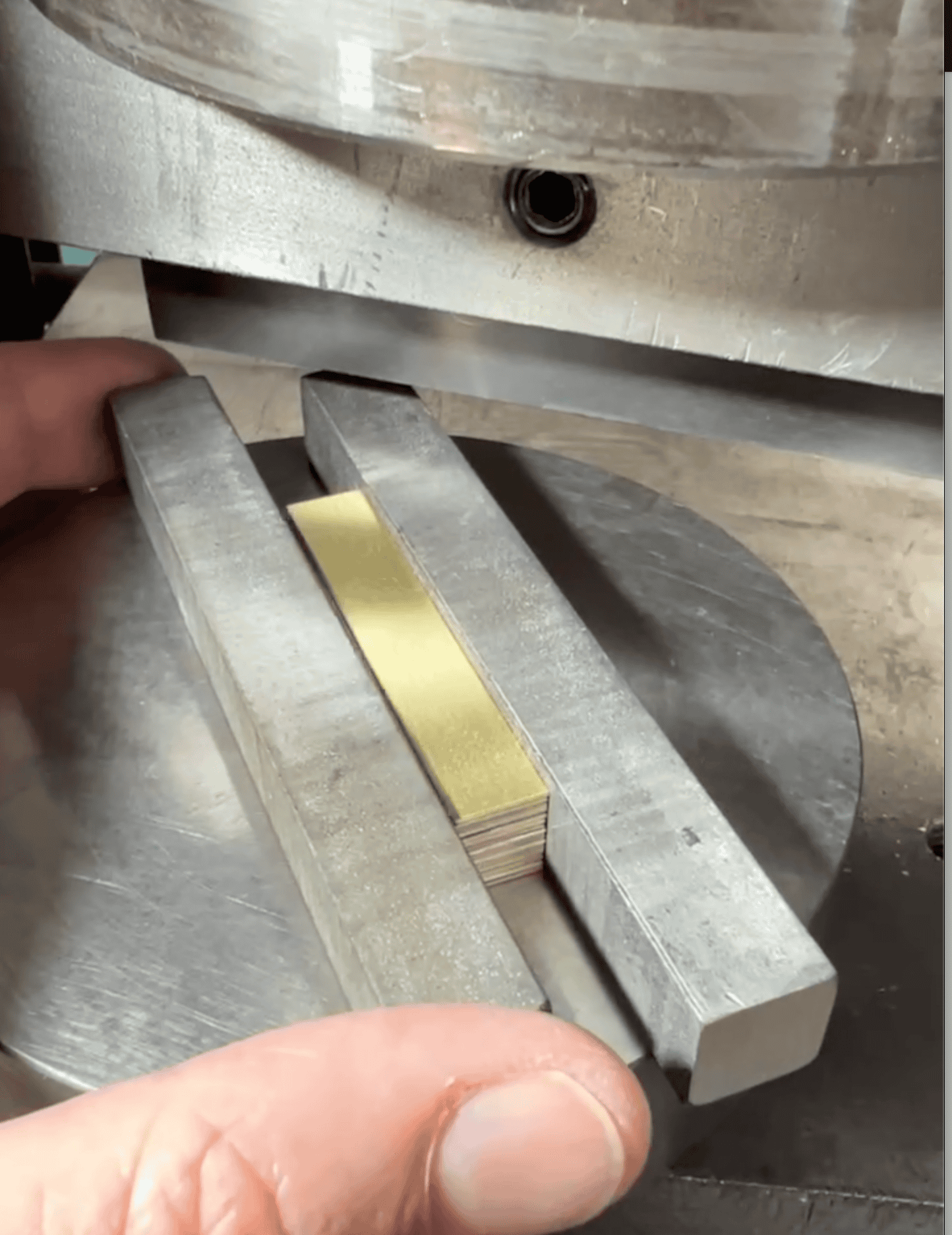 A stack made of thin metal sheets on a metal disc, being held by two metal bars, preparing to be pressed in a hydraulic press.