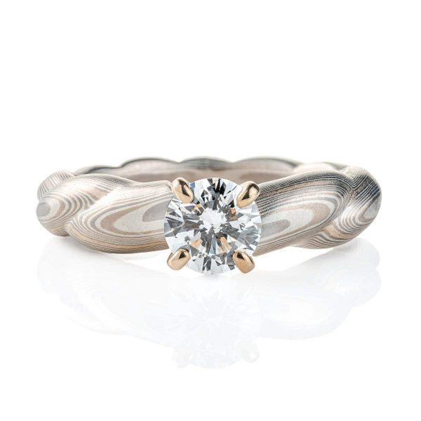 Mokume gane patterned engagement ring, carved to look like twisted rope, with a round diamond set into prongs at the top of the ring.