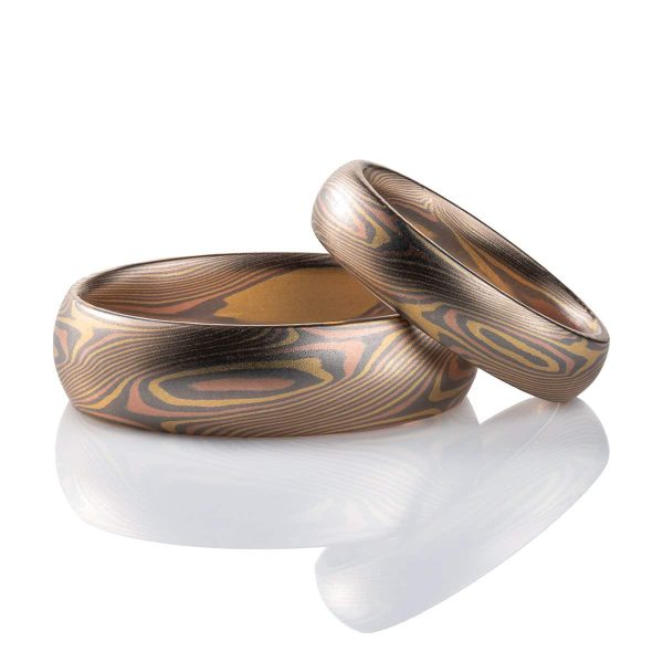 Pair of two mokume gane rings, one a larger size, one smaller, matching patterns featuring angled ellipses and diagonal lines, both made in all gold layers, domed profiles, smooth finishes.