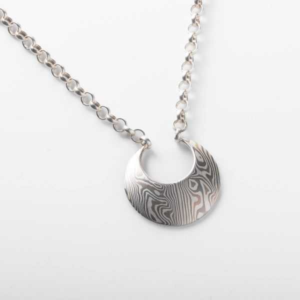 Mokume gane patterned crescent shaped pendant, with matching ring threaded through the chain and resting on top of the pendant. Made in an all silver and gray color palette.