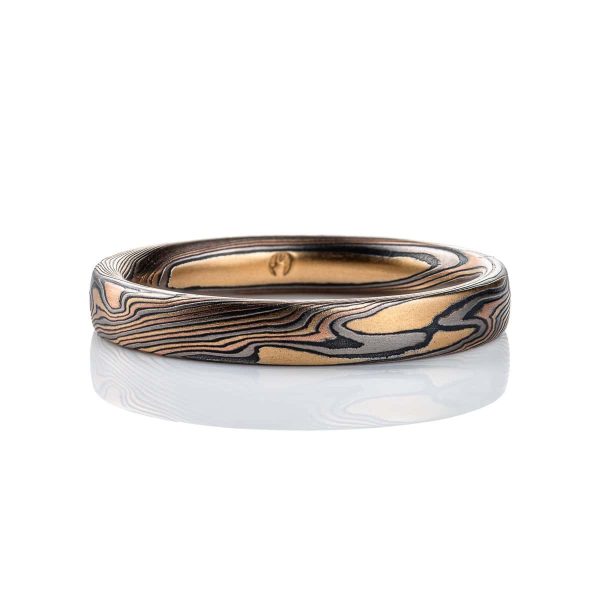 Narrow mokume gane patterned band, made with layers of red and yellow gold, palladium and oxidized silver (black), pattern is a combination of line and organic shapes.