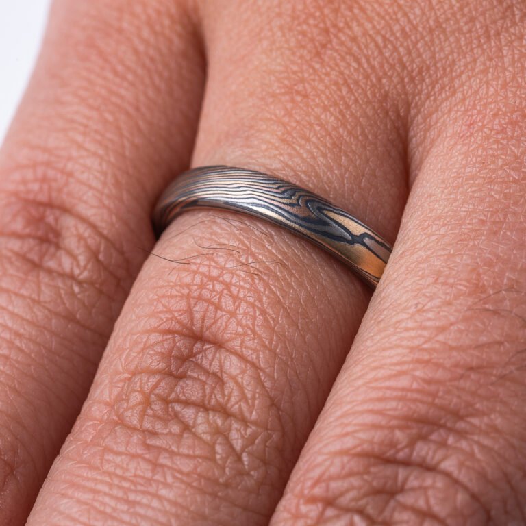 Narrow mokume gane patterned band, made with layers of red and yellow gold, palladium and oxidized silver (black), pattern is a combination of line and organic shapes.