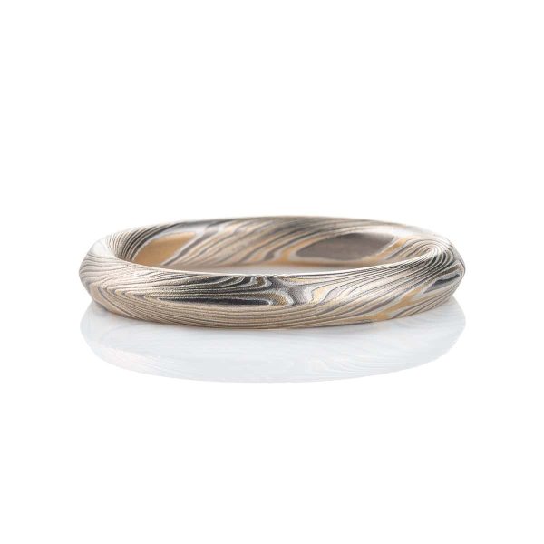 Mokume gane ring with beveled profile, patterned in long swooping lines and starburst like arcs. Made with yellow gold, silver and palladium.