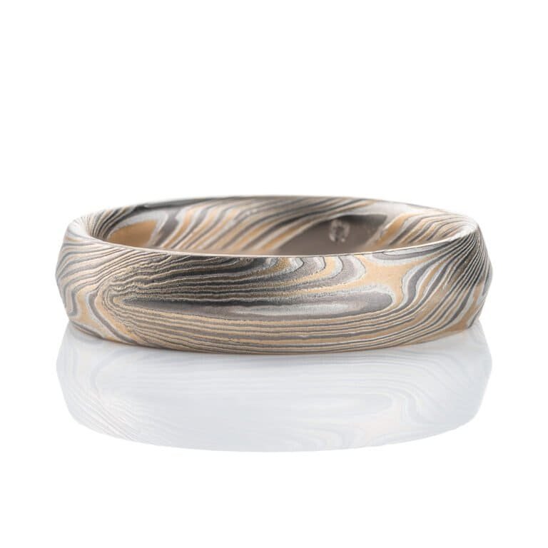 Mokume gane ring with beveled profile, patterned in long swooping lines and starburst like arcs. Made with yellow gold, silver and palladium.