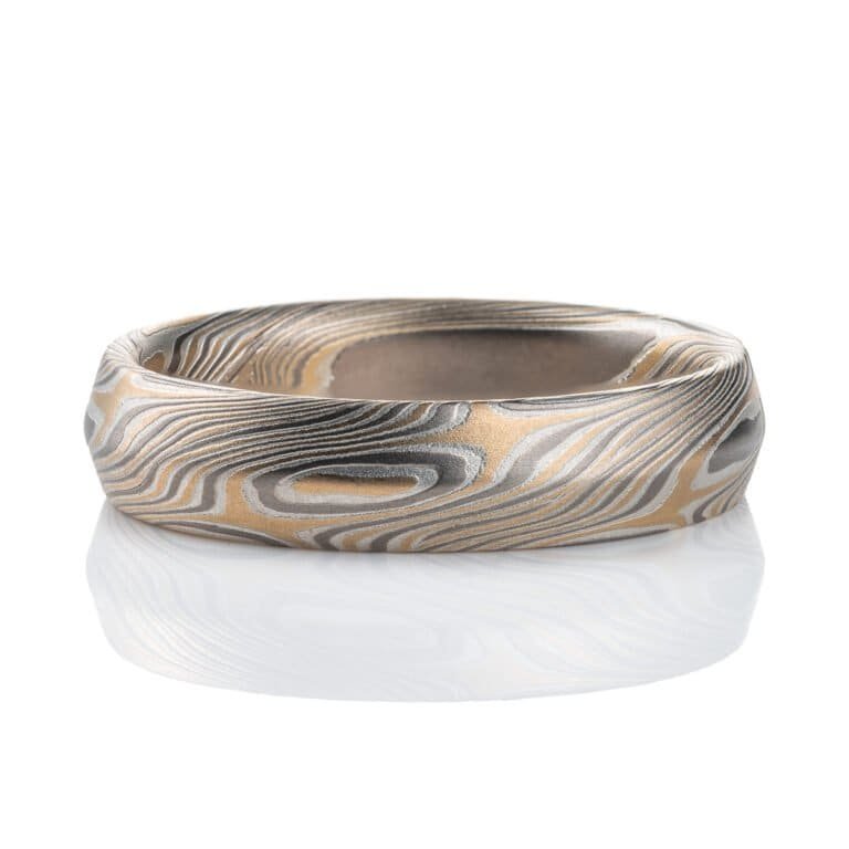 Mokume gane ring with beveled profile, patterned in long swooping lines and starburst like arcs. Made with yellow gold, silver and palladium.