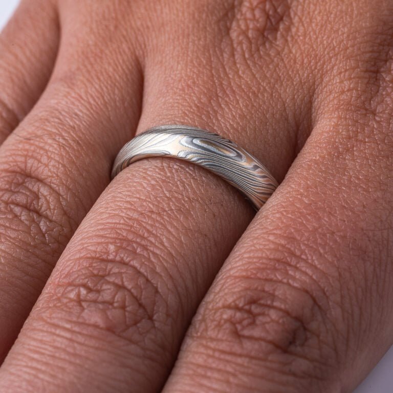 Mokume gane ring with beveled profile, patterned in long swooping lines and starburst like arcs. Made with yellow gold, silver and palladium.
