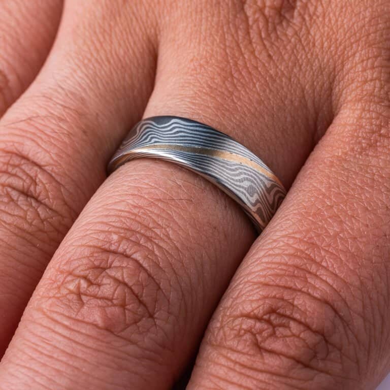 Flat profile ring made in mokume gane twist pattern, with layers of light and dark gray metals, and one layer of yellow gold.