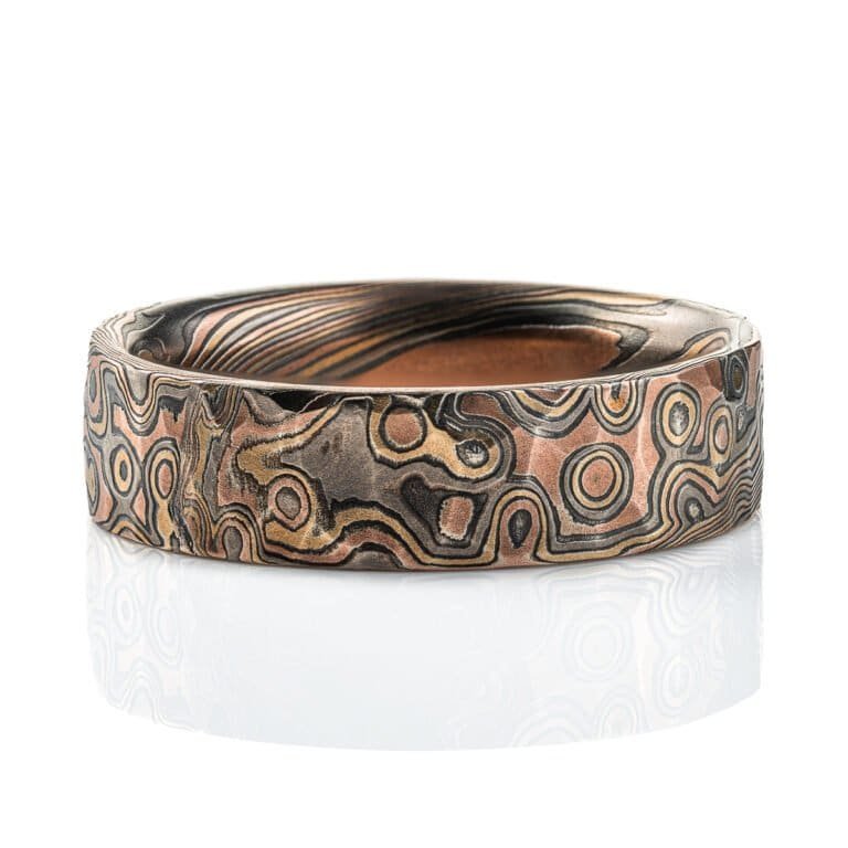 Textured mokume gane ring with flat profile, patterned in a mixture of lines and dots, and made with layers of red gold, yellow gold, palladium and oxidized silver.