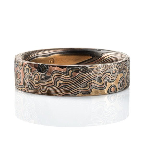 Textured mokume gane ring with flat profile, patterned in a mixture of lines and dots, and made with layers of red gold, yellow gold, palladium and oxidized silver.