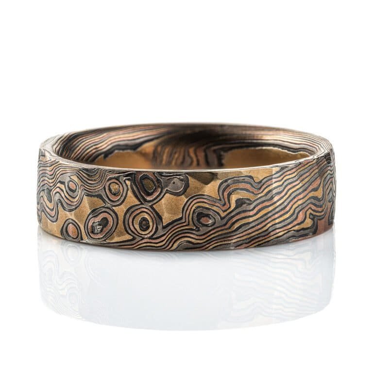 Textured mokume gane ring with flat profile, patterned in a mixture of lines and dots, and made with layers of red gold, yellow gold, palladium and oxidized silver.