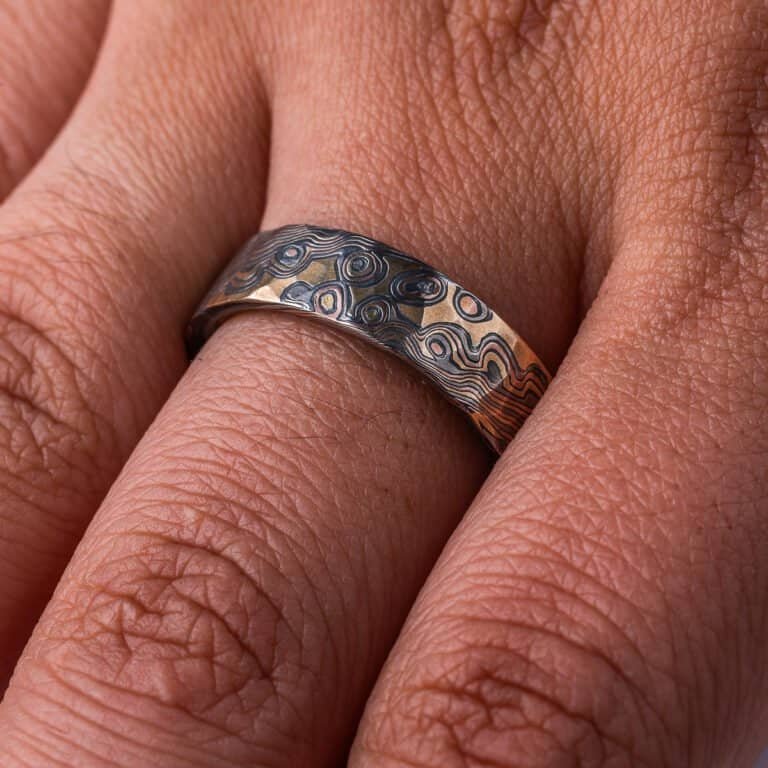 Textured mokume gane ring with flat profile, patterned in a mixture of lines and dots, and made with layers of red gold, yellow gold, palladium and oxidized silver.