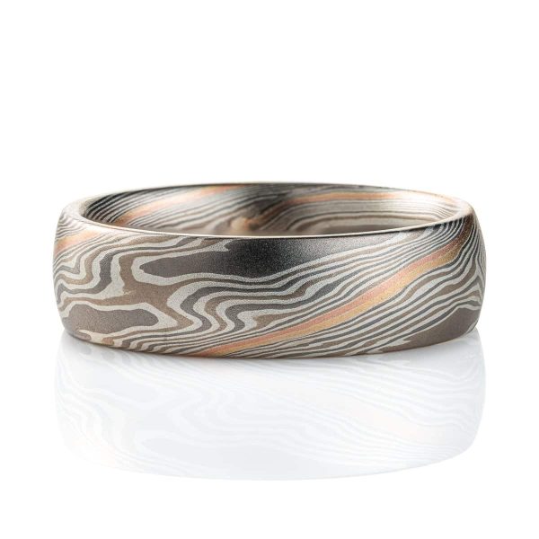 Domed mokume gane band, with a smooth surface, the ring is mainly layers of dark and light gray, with a stripe of red gold and yellow gold at the center. The lines of the pattern run diagonally across and twisting around the ring.