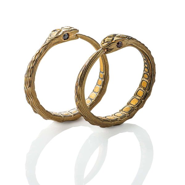 Small hoop earrings made out of mokume gane, carved to resemble snakes, with three dimensional texture, and inset stones as eyes.