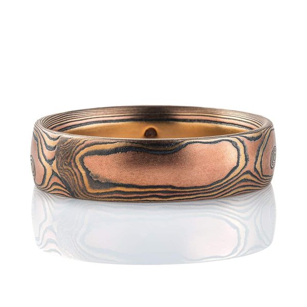 Warm toned mokume gane ring, patterned to look like woodgrain, primarily red gold in color, with yellow gold and oxidized silver (black).