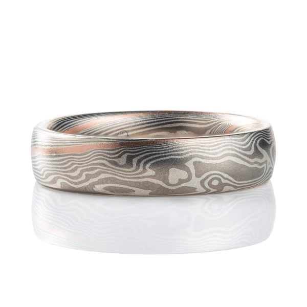Smooth, domed, slender band patterned in mokume gane twist style, most of the ring is made in silver and palladium, with one stripe of red gold.