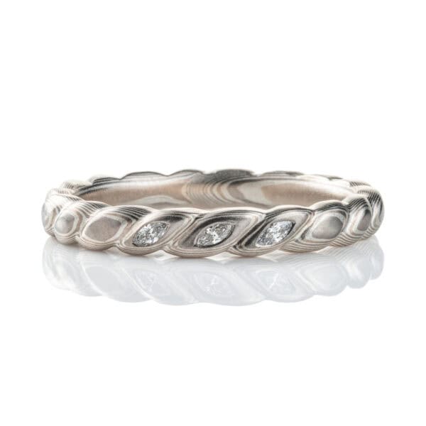 Mokume gane band carved to resemble a twisted rope, with three small flush set marquise shaped diamonds. The ring is overall silver in color palette.