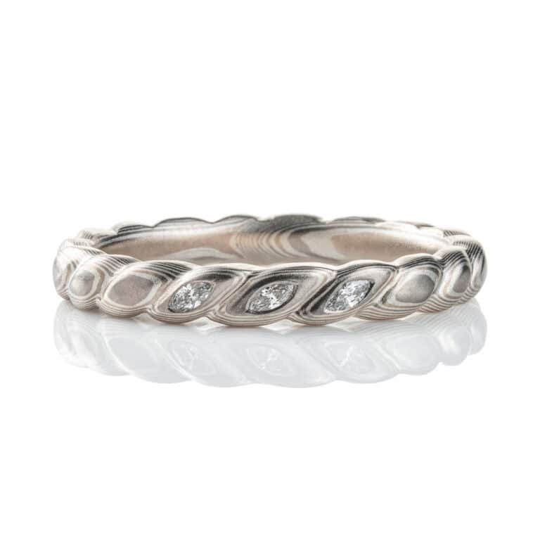 Mokume gane band carved to resemble a twisted rope, with three small flush set marquise shaped diamonds. The ring is overall silver in color palette.