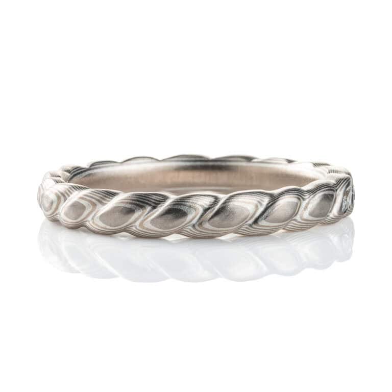 Mokume gane band carved to resemble a twisted rope, with three small flush set marquise shaped diamonds. The ring is overall silver in color palette.