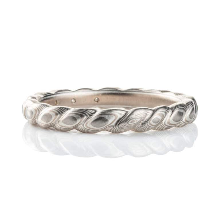 Mokume gane band carved to resemble a twisted rope, with three small flush set marquise shaped diamonds. The ring is overall silver in color palette.