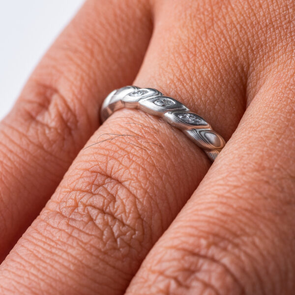 Mokume gane band carved to resemble a twisted rope, with three small flush set marquise shaped diamonds. The ring is overall silver in color palette.