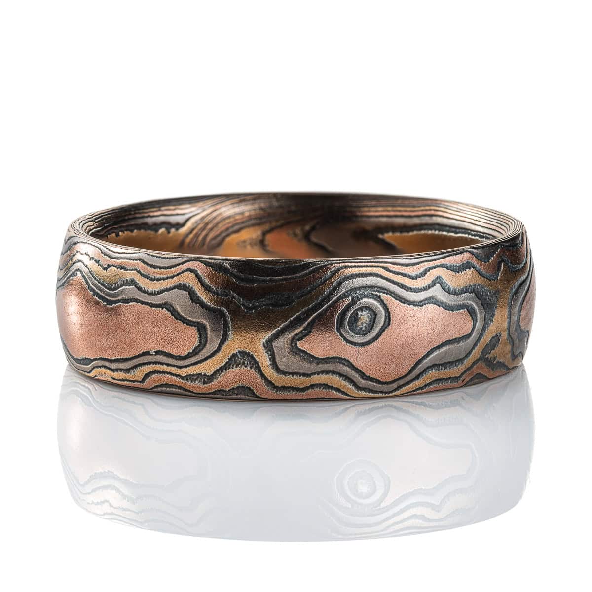 Warm toned mokume gane ring patterned to resemble wood, made with red gold, yellow gold and oxidized silver.