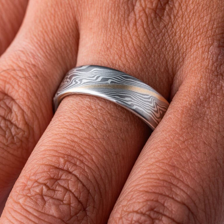 Wide flat profile mokume gane ring, patterned in twisting style, made with layers of palladium and silver for an overall gray palette, with one stripe of yellow gold.