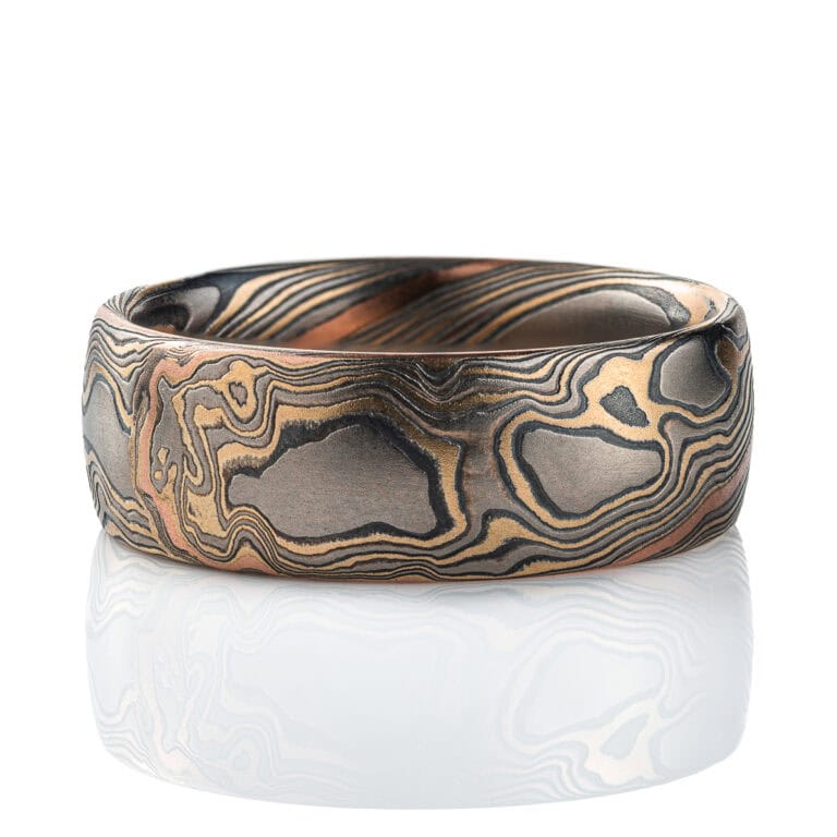 Wide men's style mokume gane band, patterned in twisting style, made with mainly yellow gold, palladium and oxidized silver, with one stripe of red gold.