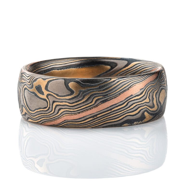 Wide men's style mokume gane band, patterned in twisting style, made with mainly yellow gold, palladium and oxidized silver, with one stripe of red gold.