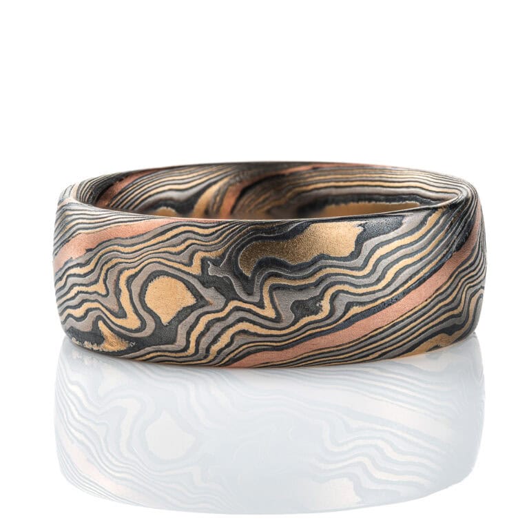 Wide men's style mokume gane band, patterned in twisting style, made with mainly yellow gold, palladium and oxidized silver, with one stripe of red gold.