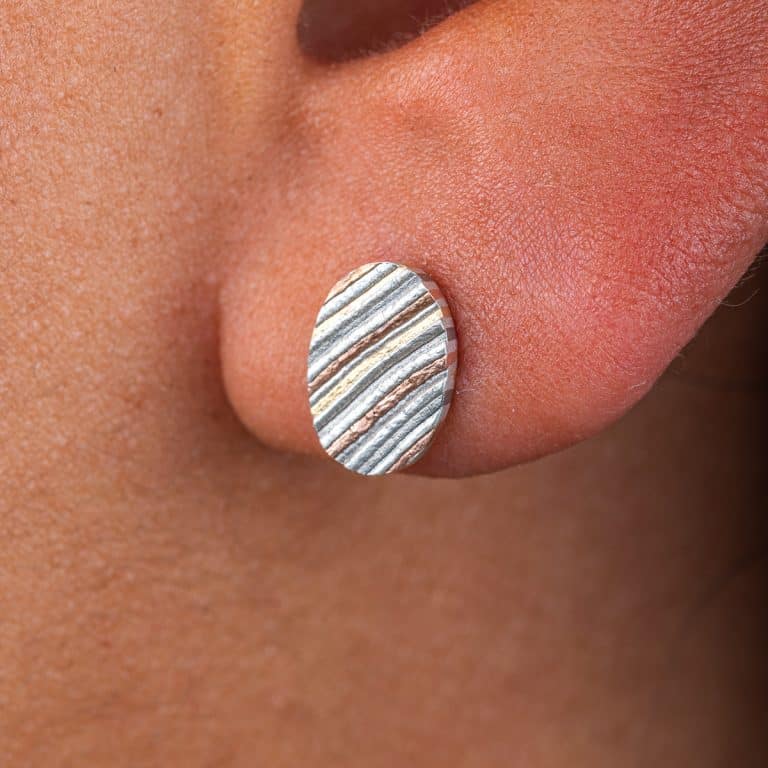 Mokume gane circular earrings patterned in a linear style, made with layers of red gold, yellow gold, palladium and silver.