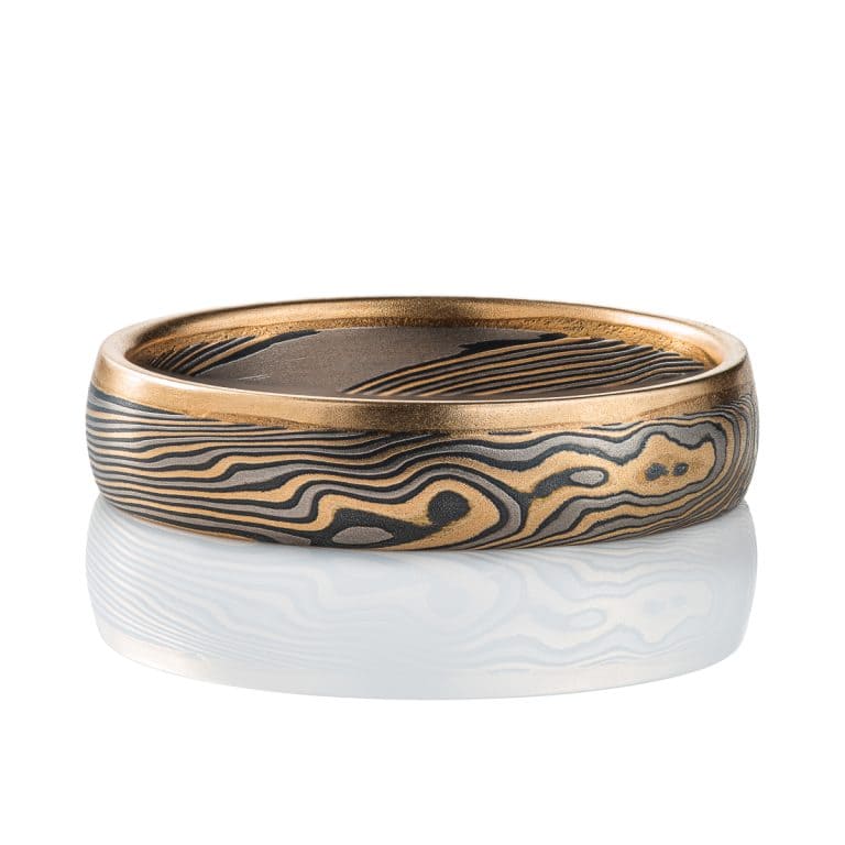 Mokume gane twisted band, with one solid strip of yellow gold running around one edge. The rest of the ring is made of layers of yellow gold, palladium and silver.