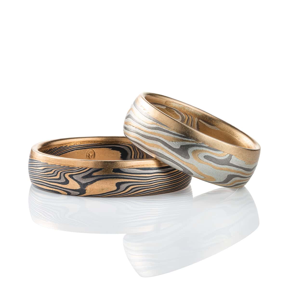 Pair of mokume gane rings, one lighter in color and wider, one darker in color and narrower, both made in a combination of yellow gold, palladium and silver, and each edged with yellow gold on one edge.