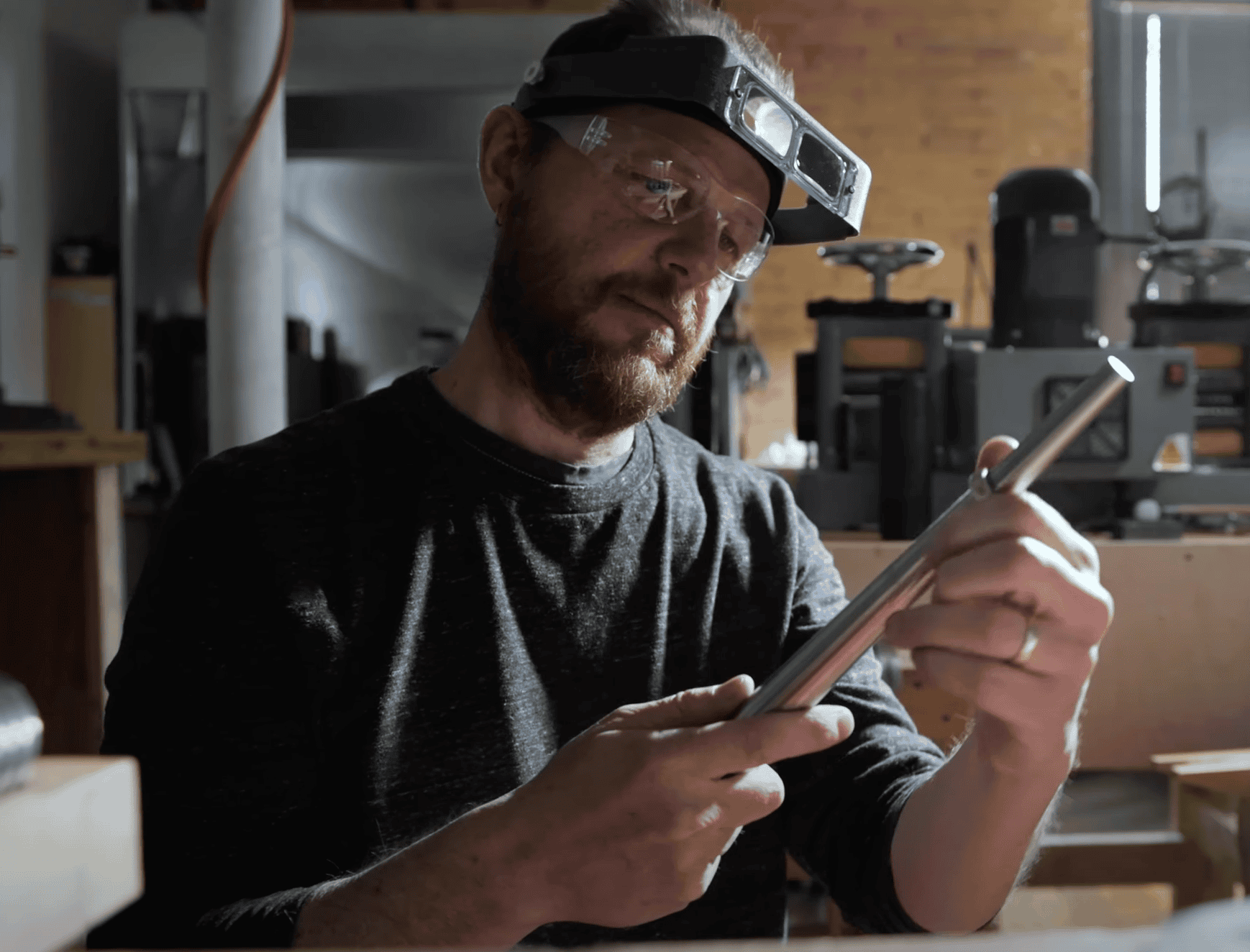 Arn Krebs, a man, in his metalsmithing workshop, holding a ring on a ring mandrel with both hands, looking at it.