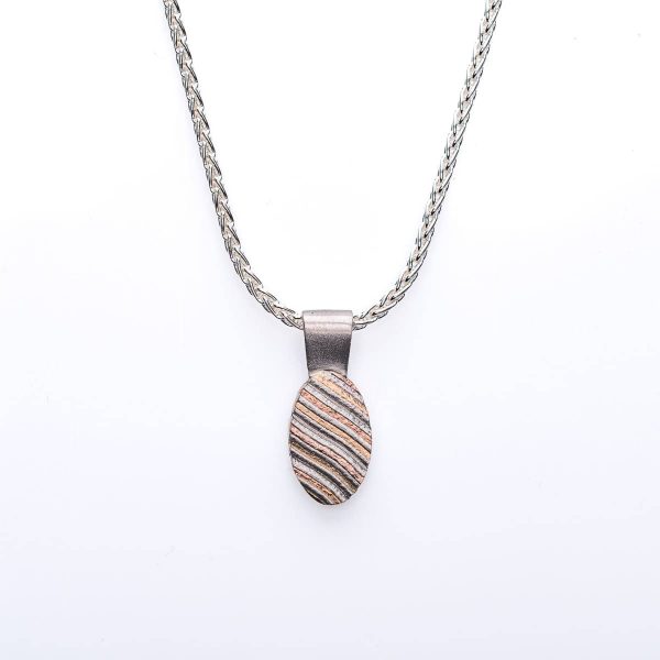 Small mokume gane patterned pendant, oval shaped, hanging on a chain. The pattern resembles stripes running diagonal across the pendant.