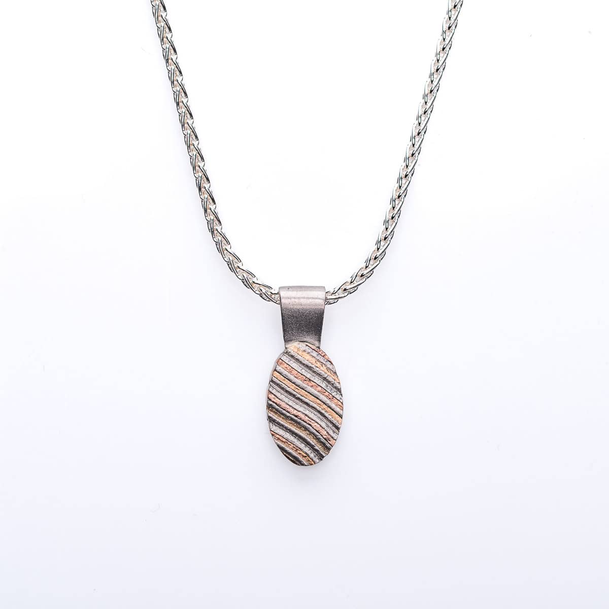 Small mokume gane patterned pendant, oval shaped, hanging on a chain. The pattern resembles stripes running diagonal across the pendant.