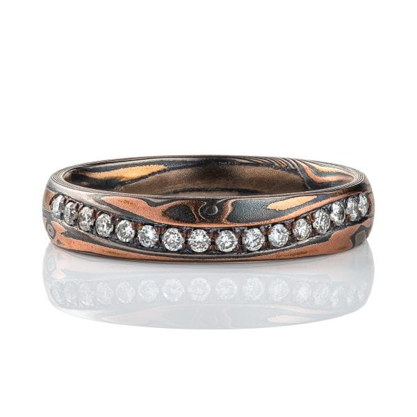 Narrow mokume gane patterned band with undulating line of diamonds set flush into the surface. The band is made of warm toned metals in a woodgrain style pattern. .