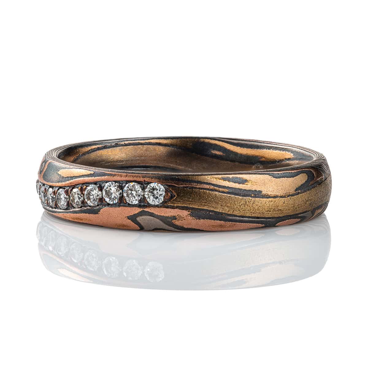 Narrow mokume gane patterned band with undulating line of diamonds set flush into the surface. The band is made of warm toned metals in a woodgrain style pattern. .