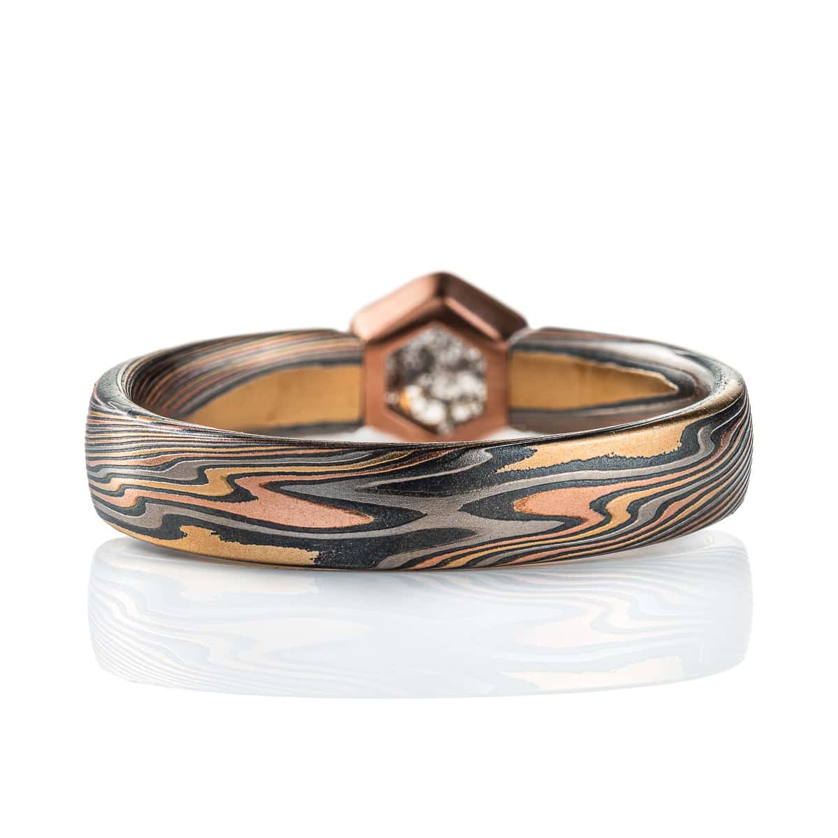 Mokume gane ring with a hexagonal stone held in a red gold bezel. The ring is made in a combination of red and yellow gold, palladium and silver. The stone is a salt and pepper diamond, with a speckled gray color.