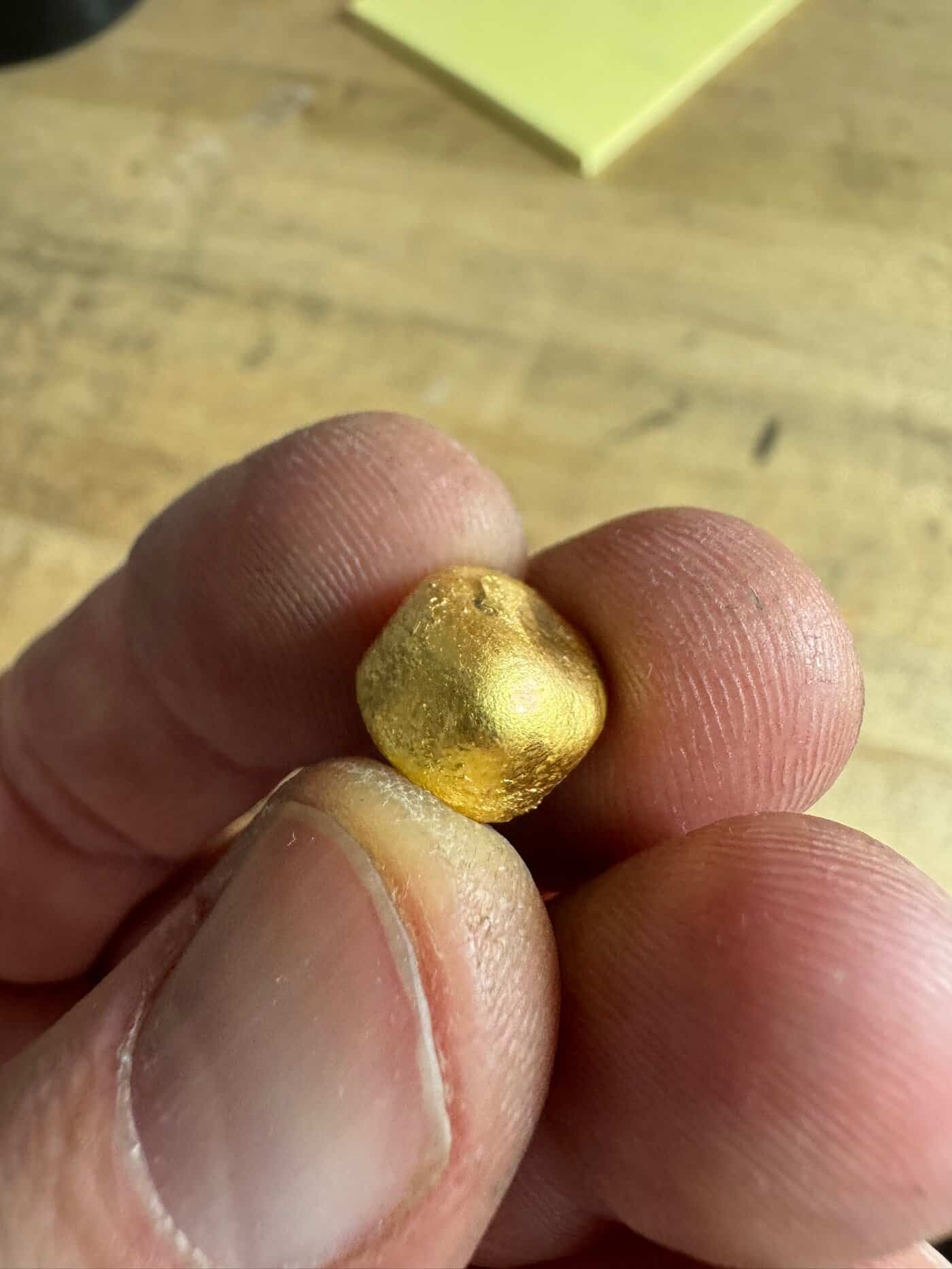 close up photo of fingers holding a small ball of gold