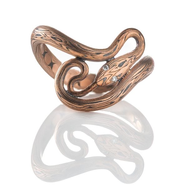 Custom handcrafted and forged mokume gane ring made to look like a snake curling and twisting around the finger. Made with red gold and oxidized silver, with tiny diamonds as eyes.
