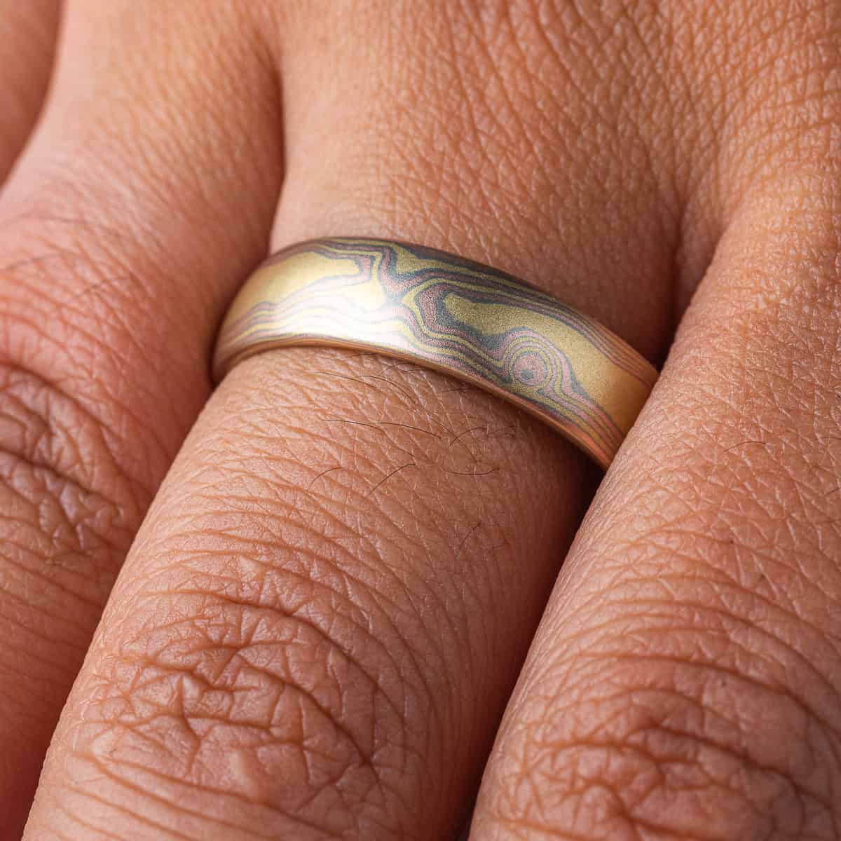 All gold mokume gane patterned band, made to resemble woodgrain, with layers of red and yellow gold with palladium in between.