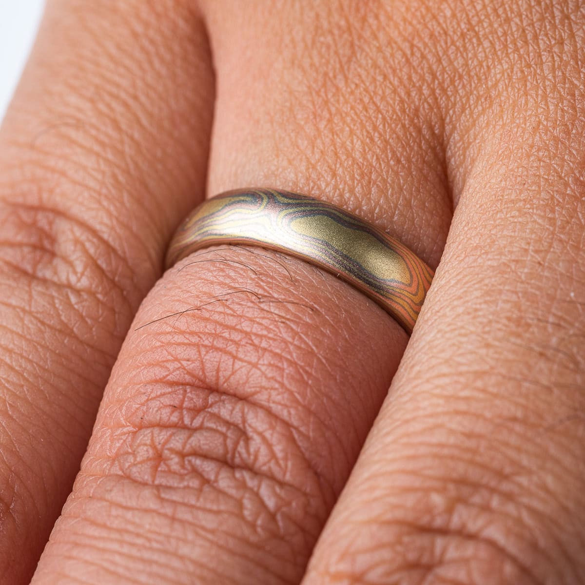 All gold mokume gane patterned band, made to resemble woodgrain, with layers of red and yellow gold with palladium in between.