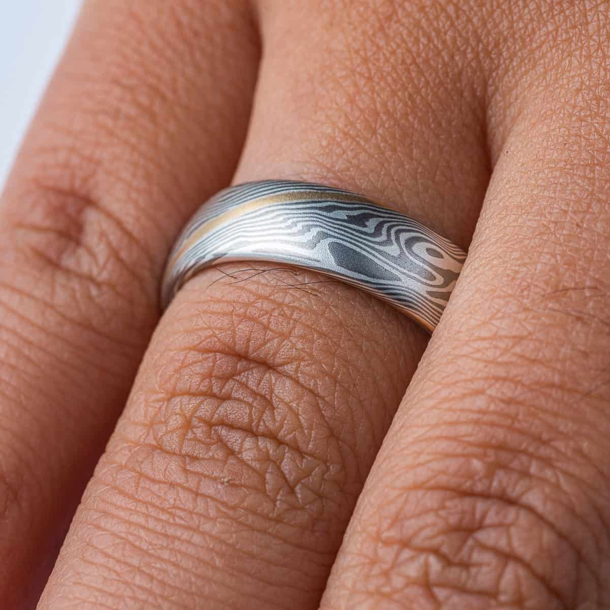 Mokume gane patterned ring made in a silver and gray color palette with a single stripe of yellow gold.