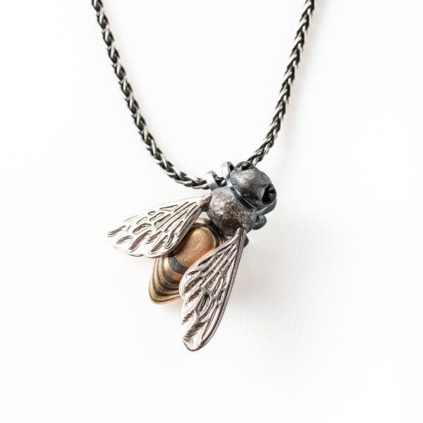 Mokume gane hand crafted honey bee pendant. Hanging from a chain by its' legs and with its' wings facing out.