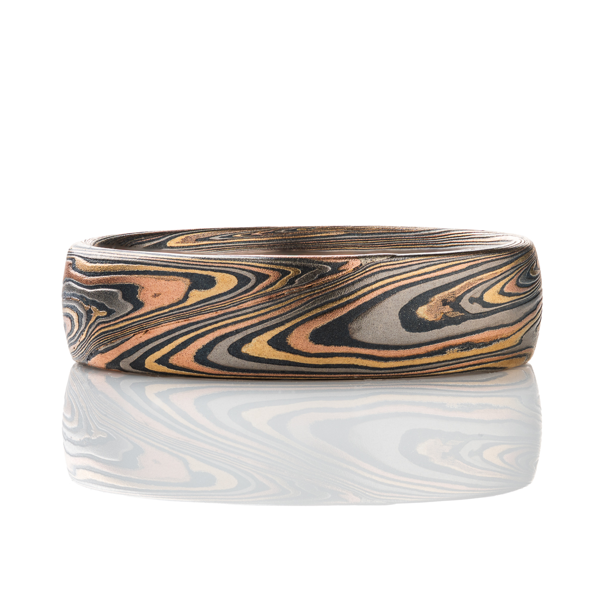 Patterned mokume gane men’s ring, made with red gold, yellow gold, palladium and oxidized silver. The pattern is organic feeling, swirling, sweeping lines.