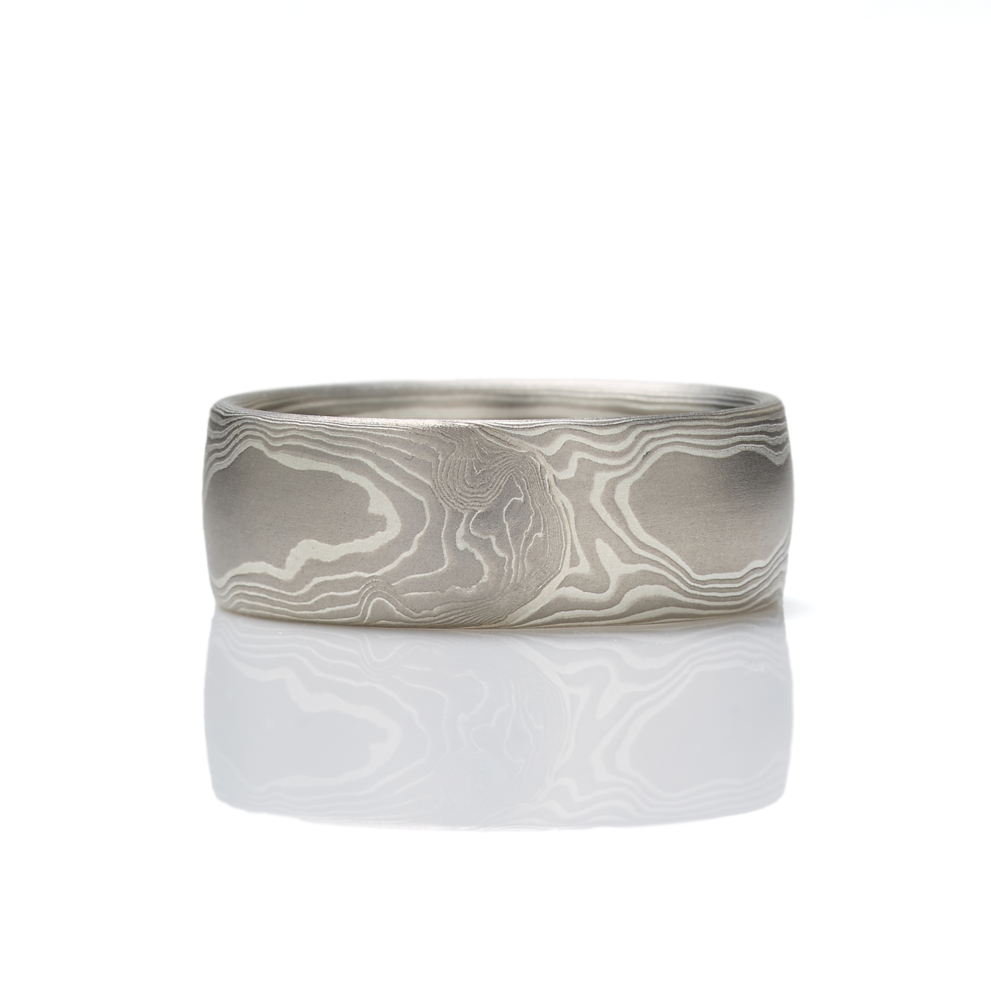 Mokume gane ring patterned in a classic woodgrain style, made with layers of palladium and silver, lightly etched for a slight texture, wide to suit a men's style, and with a low dome profile.